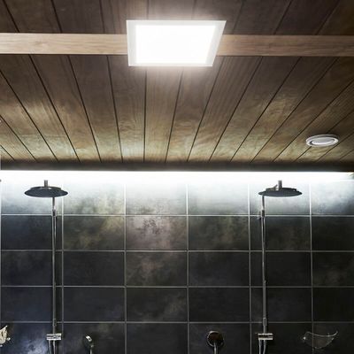 Puupaneloitu katto, jossa upotetut LED-valot, jotka valaisevat kaksinkertaiset sadesuihkupäät tyylikkäällä kaakeloidulla kylpyhuoneen seinällä.
